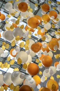 arrangement of orange, white, and yellow balloons hanging in an indoor celebration space.